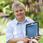 Handicapped boy holding tablet outdoors.