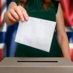 Kvinnens hånd dropper stemmeseddelen i konvolutt inn i valgurnen